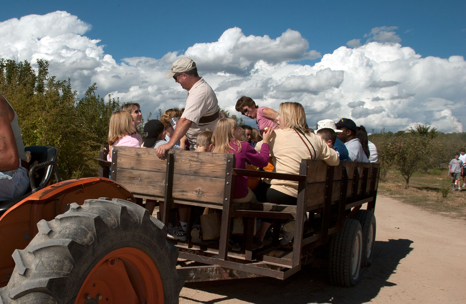An orange tractor pulls a wood wagon-style trailer through an orchard near Pueblo, Colorado. The wagon is filled with adults and children.