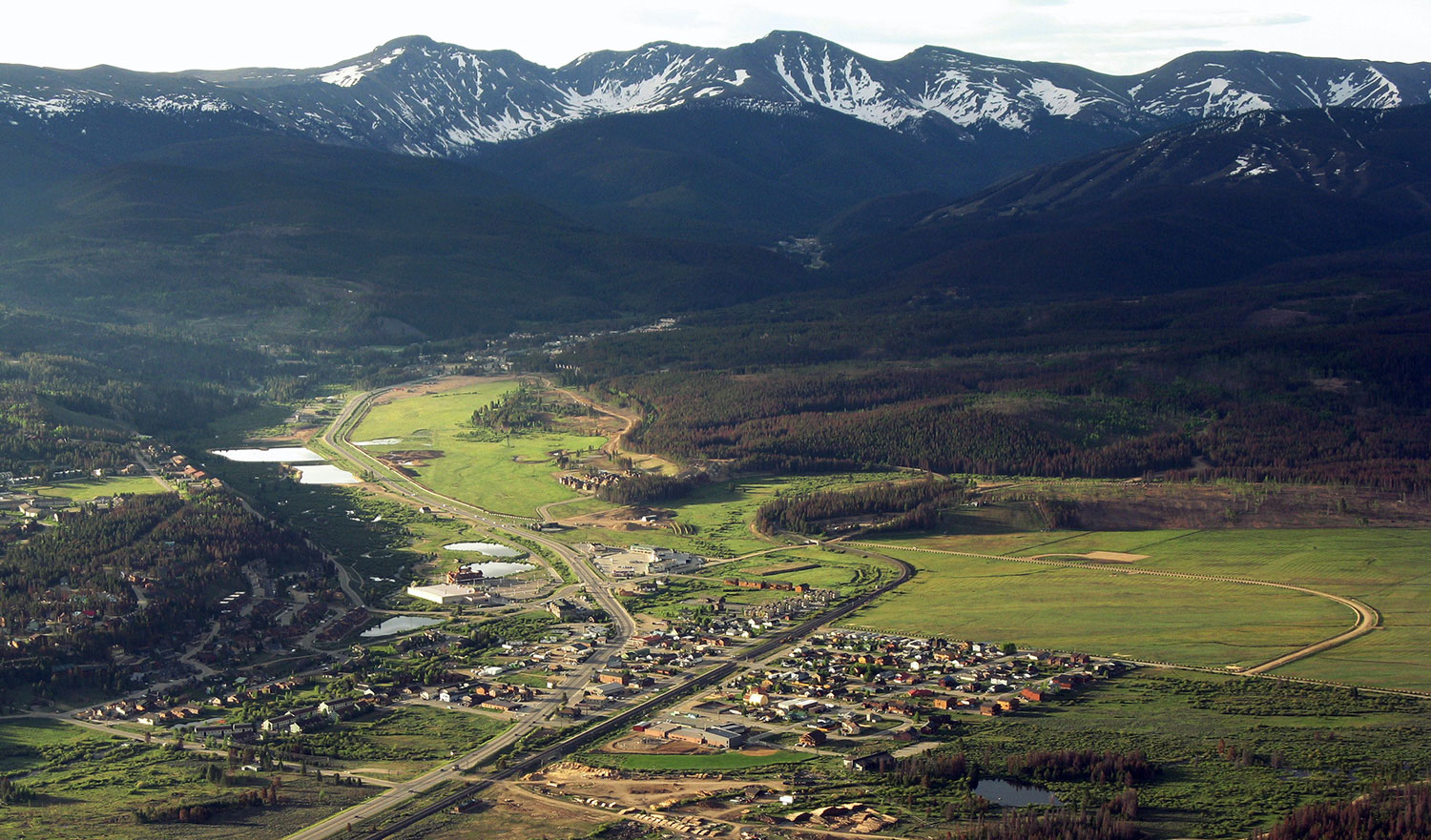 A summer aerial view of  Fraser with snow-dusted mountains in the background.