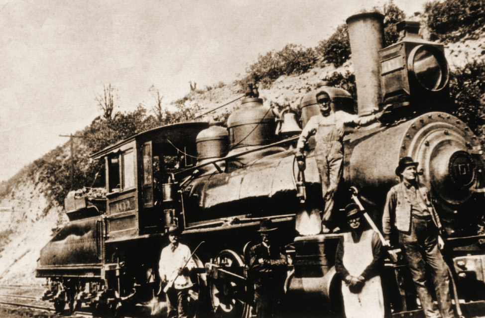 A black-and-white historic photo of a man sitting on a locomotive