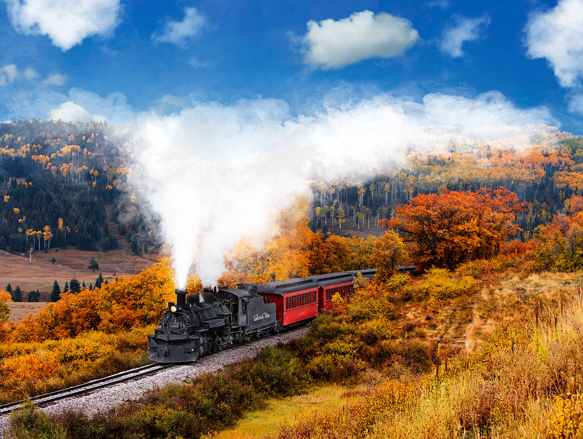 A train steams through a mountain pass full of colorful foliage