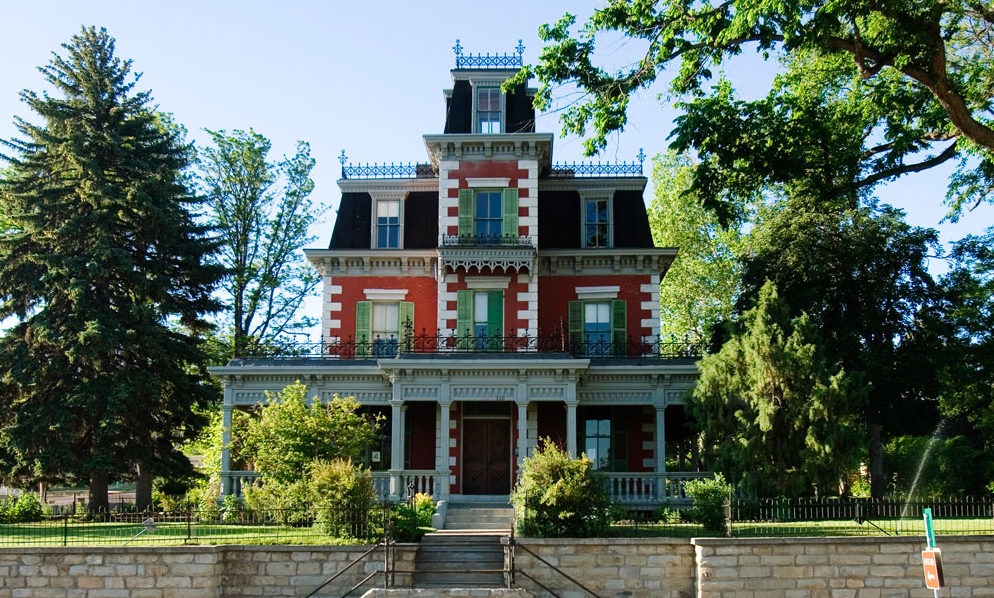 A striking three-story mansion with a decorative white-stone design, a wraparound covered porch and decorative metalwork sits in a lush park in Trinidad, Colorado.