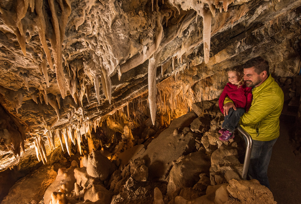 A man holds up a child to look at formations inside a cave