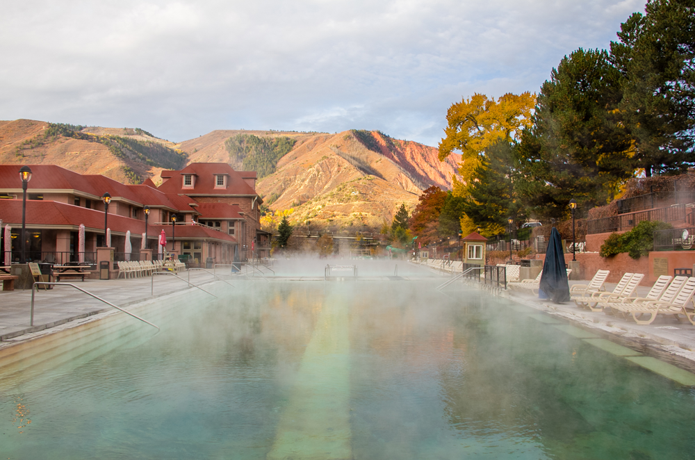 A hot springs pool with steam rising above it and mountains surrounding it